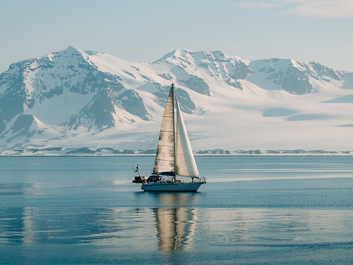 sail boat sails on a smooth sea with a snowy mountain range in the background