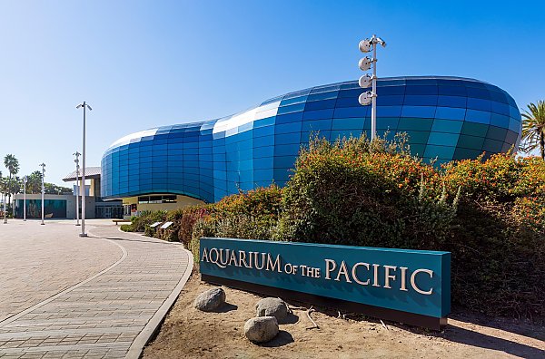 Aquarium of the Pacific sign out in front with a building with blue glass panels