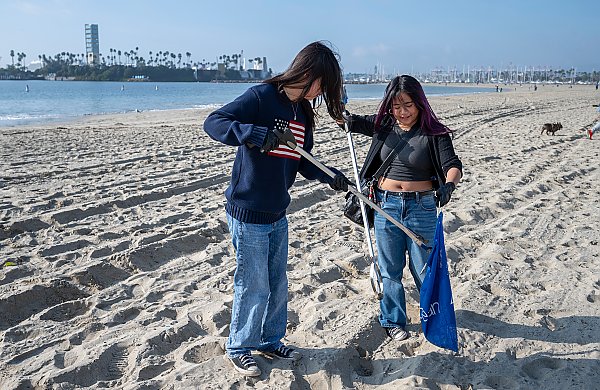 two people using long, silvery-colored grabbers to collect trash in a blue bag