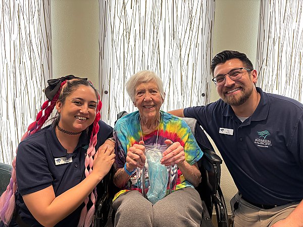 Three people smiling with the center person holding an award