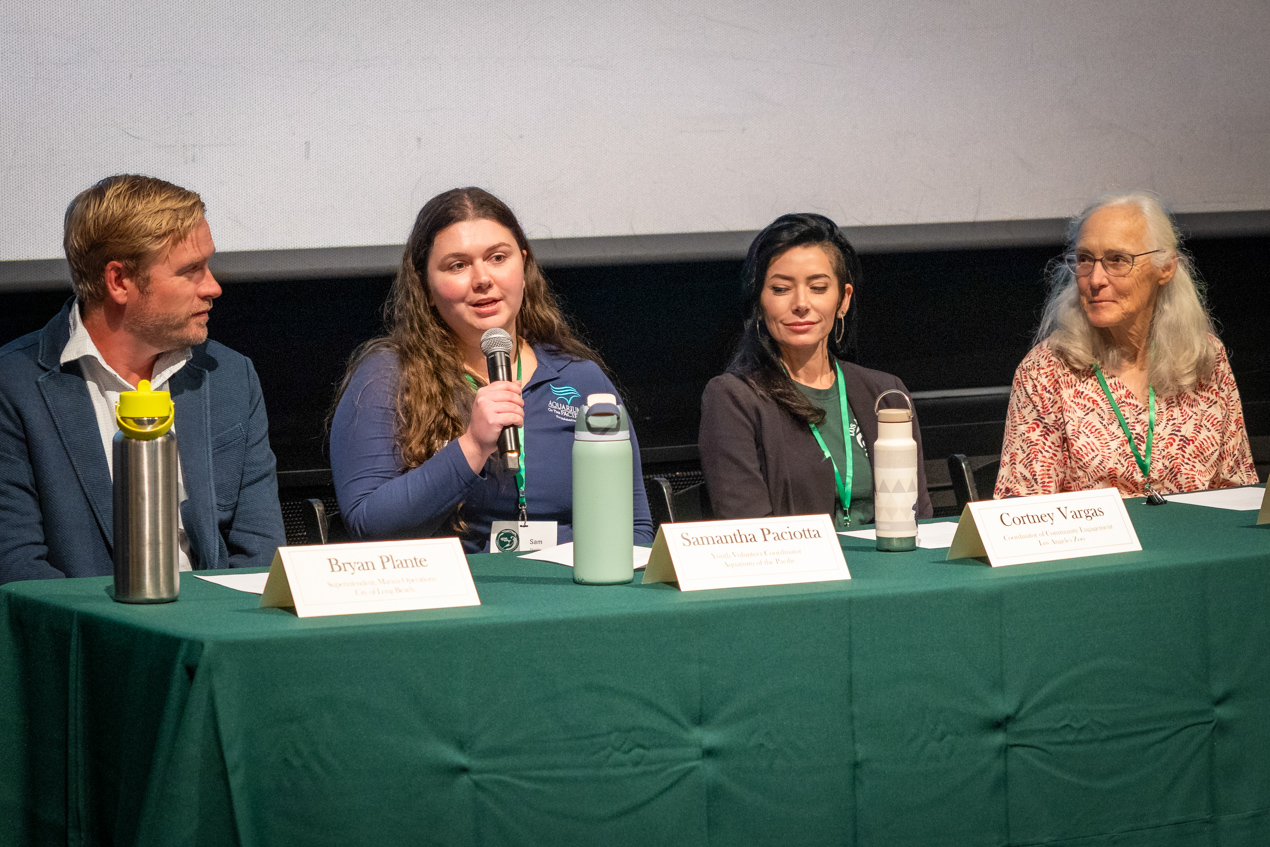 Four people at table speaking to crowd