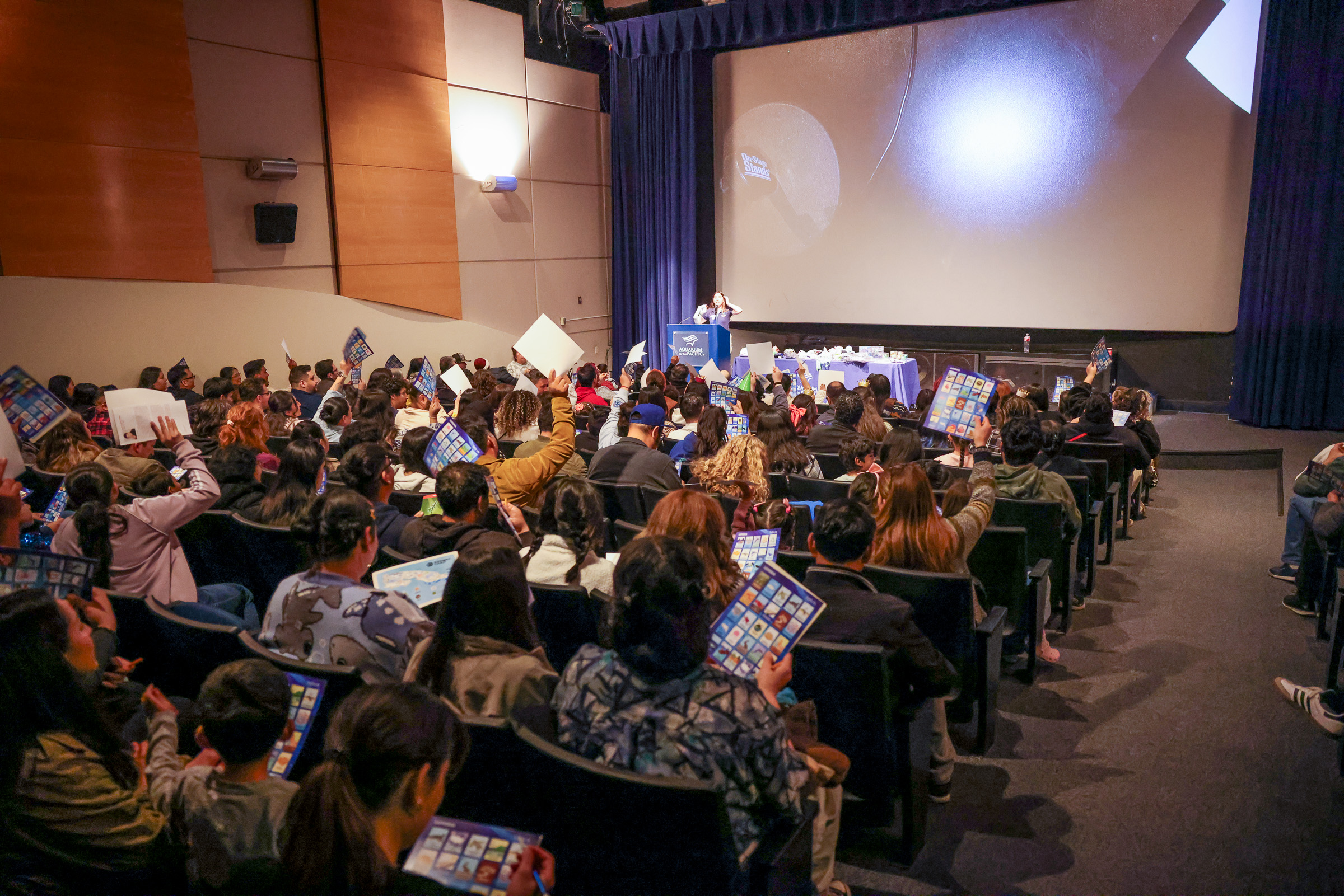 Crowded theater with people holding signs facing screen