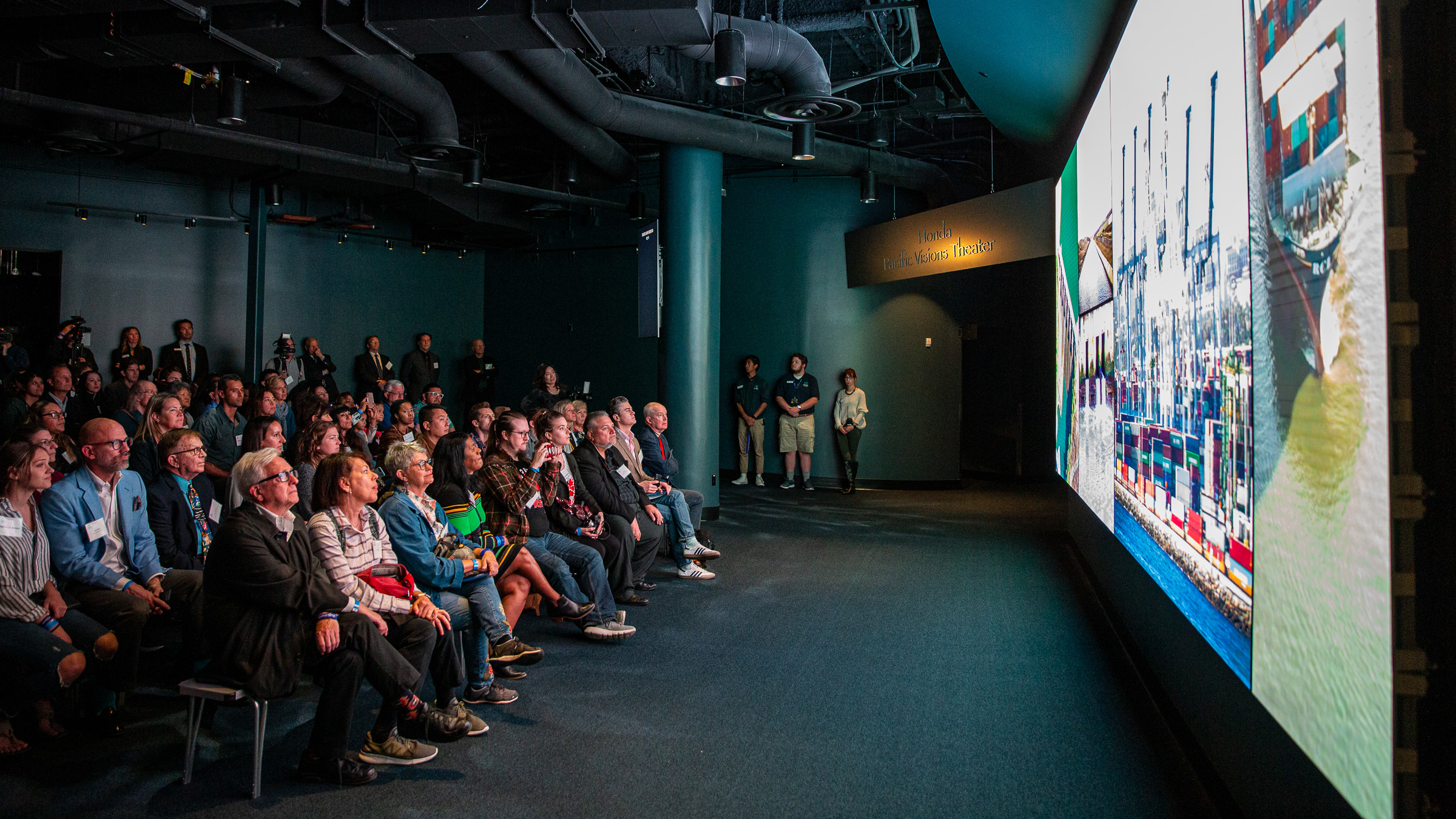 A large group of people watching a presentation on a large screen.